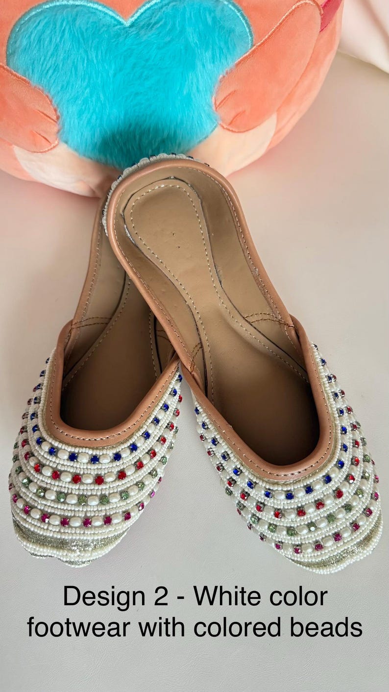 May include: White footwear with colorful bead embellishments. The shoes have a light brown interior and a white exterior adorned with red, blue, and green beads. The text on the image reads: Design 2 - White color footwear with colored beads.