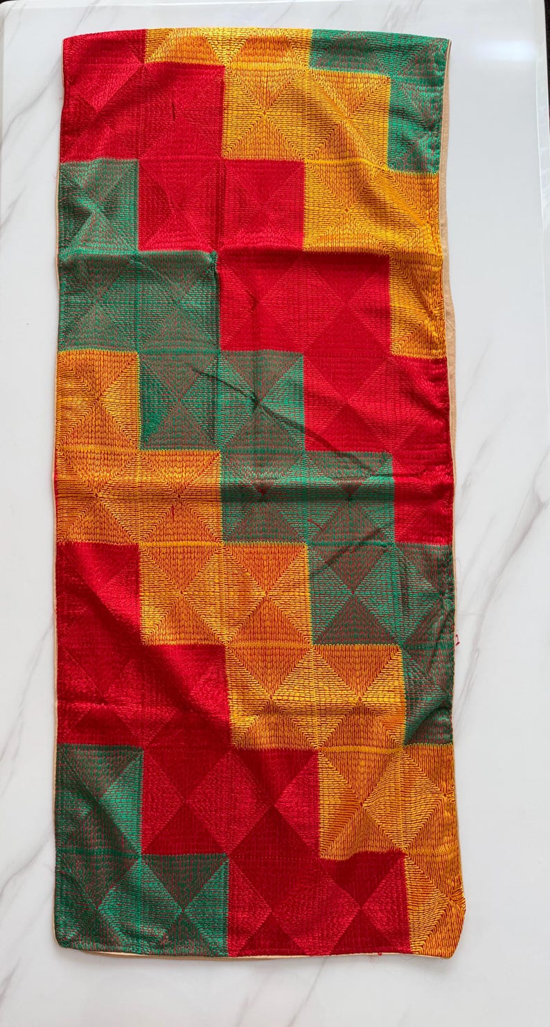 May include: A rectangular textile runner featuring a geometric grid pattern composed of alternating squares in vibrant red, golden yellow, and deep green. Each square contains intricate, fine-stitched diagonal lines forming a subtle pyramid texture.