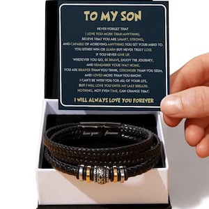 May include: A black leather bracelet with a braided design, presented in a gift box. The bracelet features silver and gold-coloured accents. A card inside the box reads "TO MY SON" with a heartfelt message.