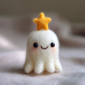 May include: A handmade felt ghost figure with a smiling face, rosy cheeks, and black bead eyes. A small, yellow star sits atop the ghost's head. The ghost has a rounded body and a small, tentacled base.