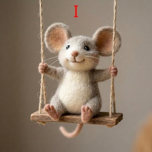 May include: A handcrafted felt mouse with a cheerful expression sits on a wooden swing suspended by twine. The mouse has gray fur, large ears, and a pink tail. The swing is made of a small piece of wood.