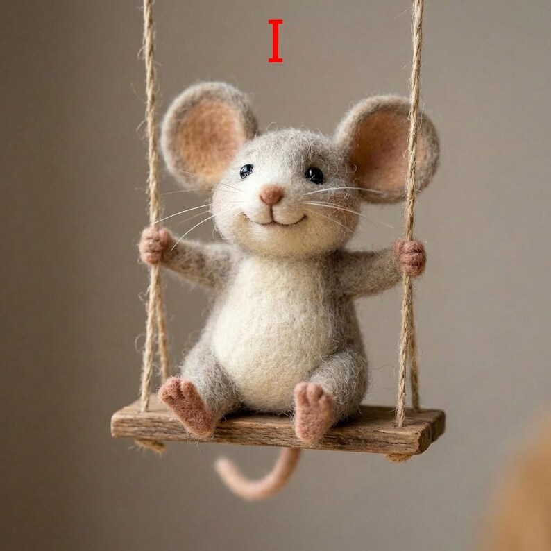May include: A handcrafted felt mouse with a cheerful expression sits on a wooden swing suspended by twine. The mouse has gray fur, large ears, and a pink tail. The swing is made of a small piece of wood.