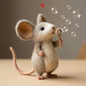 May include: A handcrafted felt mouse figurine blowing bubbles. The mouse is light brown with large ears and a long tail. It holds a bubble wand, and several clear bubbles float in the air. The letter "K" is in the upper left corner.