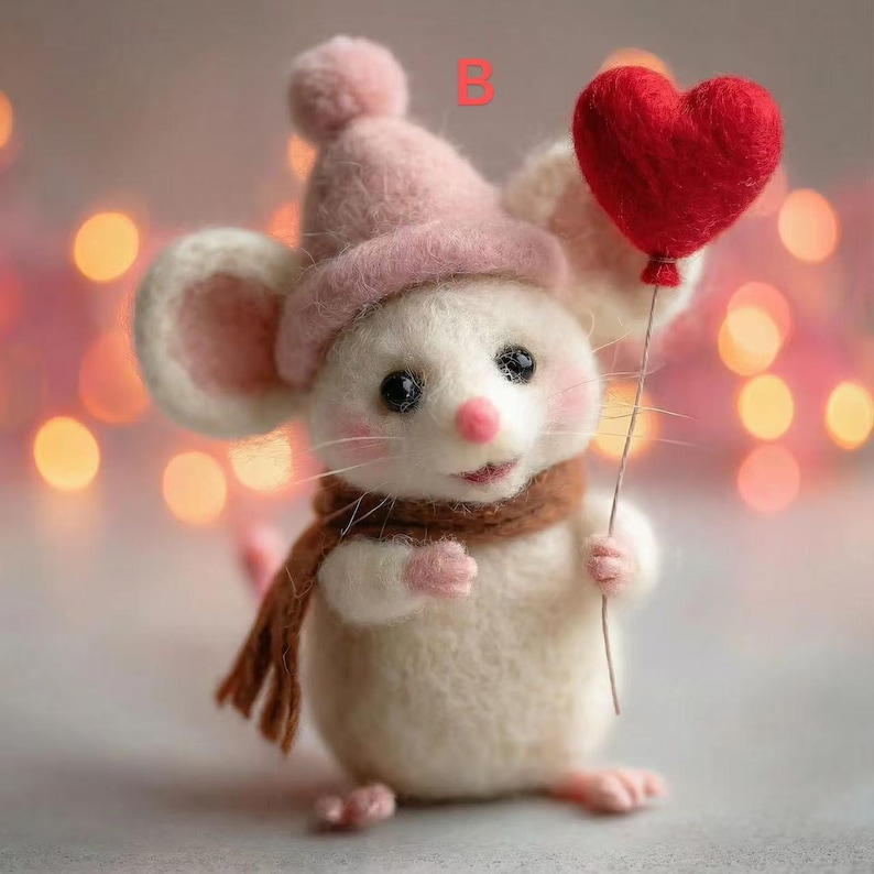 May include: A handcrafted white mouse figurine wearing a pink hat and brown scarf, holding a red heart-shaped balloon. The mouse has black eyes, a pink nose, and rosy cheeks. The background features soft, blurred bokeh lights.