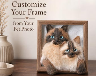 Op de afbeelding: Een vierkante houten lijst met een 3D-portret van naaldvilt van twee katten met blauwe ogen en bruin en crème gekleurde vacht. De tekst Customize Your Frame from Your Pet Photo staat in bruin boven de lijst naast een kleine vaas.