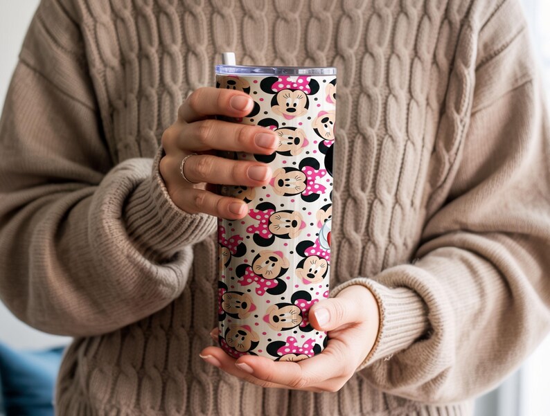 K&ouml;nnte beinhalten: Ein Edelstahlbecher mit einem sich wiederholenden Muster von Minnie Mouse-Gesichtern mit rosa Schleifen auf cremefarbenem Hintergrund. Der Becher hat einen transparenten Deckel und einen wei&szlig;en Strohhalm. Das Design ist verspielt und f&uuml;r Getr&auml;nke geeignet.