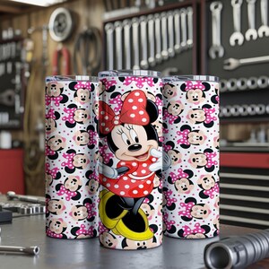 K&ouml;nnte beinhalten: Drei Edelstahlbecher mit einem Minnie-Maus-Design. Die Becher haben einen wei&szlig;en Hintergrund mit einem sich wiederholenden Muster aus Minnie-Maus-Gesichtern und rosa Schleifen. Ein Becher zeigt ein vollst&auml;ndiges Minnie-Maus-Bild in einem roten Polka-Dot-Kleid.