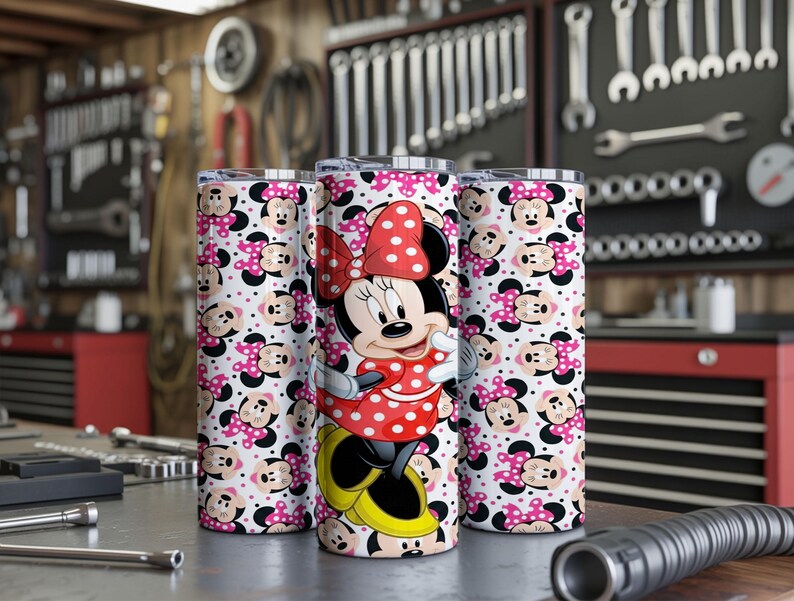 K&ouml;nnte beinhalten: Drei Edelstahlbecher mit einem Minnie-Maus-Design. Die Becher haben einen wei&szlig;en Hintergrund mit einem sich wiederholenden Muster aus Minnie-Maus-Gesichtern und rosa Schleifen. Ein Becher zeigt ein vollst&auml;ndiges Minnie-Maus-Bild in einem roten Polka-Dot-Kleid.