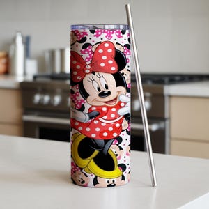 K&ouml;nnte beinhalten: Ein Edelstahlbecher mit Minnie Mouse-Design. Der Becher hat ein rot-wei&szlig;es Polka-Dot-Muster, einen Edelstahlstrohhalm und einen Hintergrund aus Minnie Mouse-Gesichtern und rosa Schleifen. H&ouml;he ca. 25 cm.