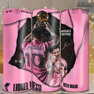 May include: A pink Inter Miami tumbler featuring Lionel Messi. The design includes images of Messi, a trophy, and the text "Impossible is Nothing." The tumbler has a silver straw and the Inter Miami logo.