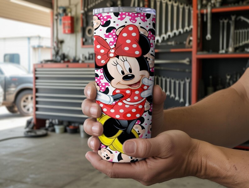 K&ouml;nnte beinhalten: Ein Edelstahlbecher mit Minnie Maus. Der Becher hat einen wei&szlig;en Hintergrund mit einem Muster aus Minnie Maus-Gesichtern und rosa Tupfen. Minnie Maus tr&auml;gt ein rotes Kleid mit wei&szlig;en Punkten und eine passende Schleife.