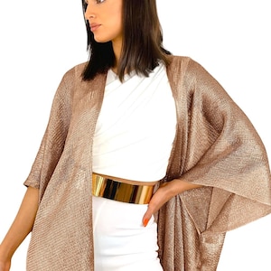 Peut inclure: Une veste kimono ouverte de couleur bronze avec des manches larges. La veste est associée à une ceinture dorée et à une tenue blanche. Le tissu a un aspect texturé, ajoutant de la profondeur au design. Le style général est élégant et moderne.