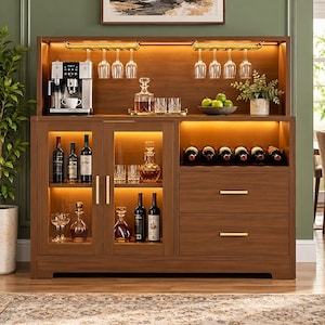 May include: A wooden bar cabinet with integrated warm LED lighting, featuring a coffee machine, glass racks with hanging stemware, a wine rack for six bottles, two glass-front doors, and two drawers with gold-toned horizontal handles.