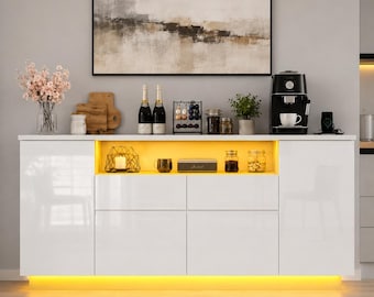 May include: A white sideboard with a glossy finish, featuring two side cabinets and two central drawers. The unit includes an open shelf with warm yellow LED lighting, displaying a wire candle holder, a mug, a box, and glass jars.