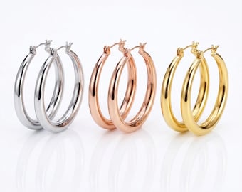 Op de afbeelding: Drie paar oorringen in zilver, roségoud en goud. De oorbellen zijn in een rij gerangschikt, elk paar met een klassiek, afgerond ontwerp. De oorbellen worden gepresenteerd tegen een witte achtergrond.
