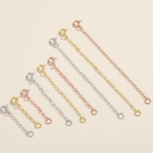 May include: A collection of necklace extender chains in silver, gold, and rose gold tones. Each chain has a lobster clasp on one end and a jump ring on the other. The chains vary in length, offering versatility for jewelry adjustments.