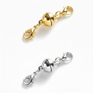 May include: Two magnetic clasps for jewelry. One is gold-toned, the other is silver-toned. Each clasp features a spherical magnetic closure and two lobster claw clasps for easy attachment to necklaces or bracelets.
