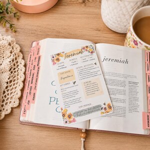 May include: A rectangular card featuring a floral Jeremiah Bible study summary with sections for author, audience, key characters, main theme, key verses, purpose, and main message, placed on an open Bible with pink tabs and a wooden bookmark.