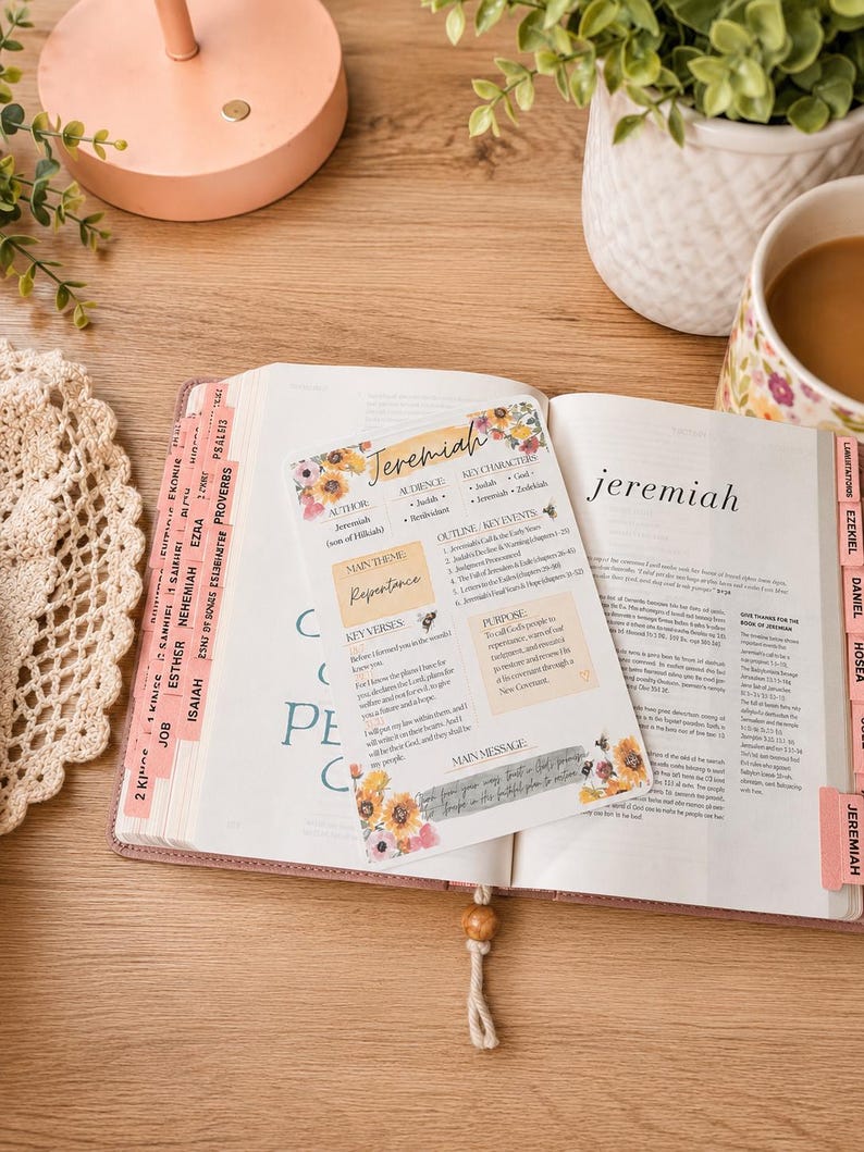 May include: A rectangular card featuring a floral Jeremiah Bible study summary with sections for author, audience, key characters, main theme, key verses, purpose, and main message, placed on an open Bible with pink tabs and a wooden bookmark.