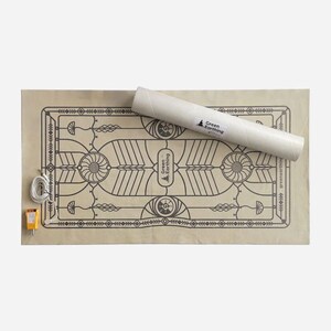 May include: A beige grounding mat with a decorative black pattern and the text "Green Earthing". A rolled-up white tube with the "Green Earthing" logo rests on the mat. A yellow and white electrical component is attached to the mat.