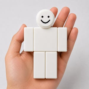 Puede incluir: Una figura blanca en forma de bloque con una cara sonriente en la cabeza. La figura est&aacute; compuesta por bloques rectangulares, que se asemejan a una forma humana simplificada. El dise&ntilde;o es minimalista y moderno, con una superficie limpia y lisa. La figura se sostiene en una mano.