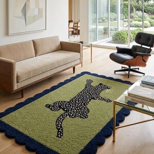 May include: A rectangular green rug with a navy blue scalloped border. The rug features a black and white leopard design in the center. The rug is placed on a hardwood floor in a living room setting.