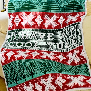 May include: A green, red, and white crocheted blanket with the text "Have a Cool Yule" in white yarn. The blanket features a repeating pattern of snowflakes, pine trees, and a festive design.