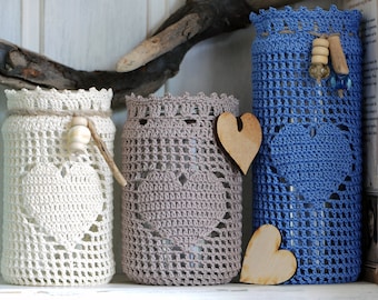 May include: Three glass jars with crocheted covers in white, gray, and blue. The jars are decorated with wooden hearts and beads.