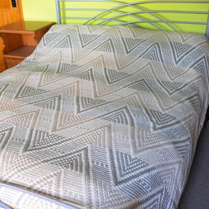 Puede incluir: Una manta de punto de chevron beige y gris sobre un marco de cama de metal.