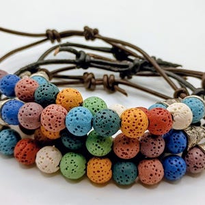 May include: A collection of beaded bracelets with colourful porous beads in shades of blue, orange, green, and red. The bracelets are strung on brown leather cords and finished with decorative metal end caps.