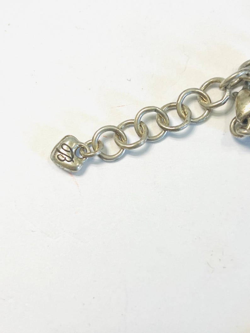 May include: A silver-toned metal chain extender featuring a series of circular links and a small heart-shaped charm at the end. The charm is embossed with the stylised letters TB in a cursive script, providing a decorative finish to the jewellery piece.