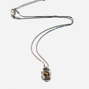 May include: Silver-toned necklace with a pendant featuring a gold-colored heart. The pendant has the words "LIVE FROM THE HEART" engraved on it. The necklace has a delicate chain and a lobster clasp.