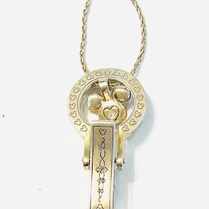 Puede incluir: Un collar plateado con un colgante tem&aacute;tico de Mickey Mouse. El colgante presenta un dise&ntilde;o circular con siluetas de la cabeza de Mickey Mouse, una cabeza de Mickey Mouse con una gema en forma de coraz&oacute;n y un dije rectangular con un patr&oacute;n adornado. La cadena es un dise&ntilde;o delicado y retorcido.