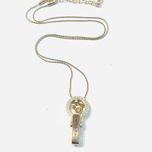 Puede incluir: Collar plateado con colgante. El colgante tiene un dise&ntilde;o de coraz&oacute;n y llave, con una barra rectangular grabada con la palabra "DAUGHTER". El collar se muestra sobre un fondo blanco.