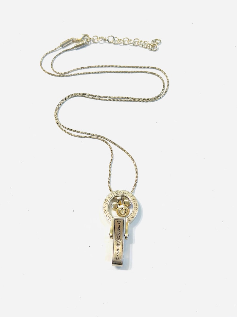 Puede incluir: Collar plateado con colgante. El colgante tiene un dise&ntilde;o de coraz&oacute;n y llave, con una barra rectangular grabada con la palabra "DAUGHTER". El collar se muestra sobre un fondo blanco.