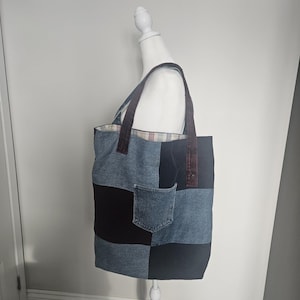 Peut inclure: Un sac fourre-tout en denim patchwork avec des poignées marron et une poche en jean. Le sac est présenté sur un mannequin blanc. Le design du sac incorpore diverses nuances de denim bleu et de tissu noir.