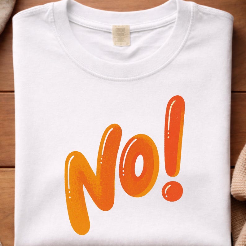 May include: White t-shirt with the word "No!" in orange, outlined in a darker orange. The exclamation point is a tall, vertical line with a small circle at the bottom. The shirt has a crew neck and a tag.