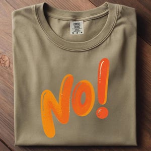 May include: A folded, olive-green t-shirt with the word "NO!" in large, orange, bubble letters. The exclamation point is also orange. The shirt has a tag that reads "Comfort Colors".