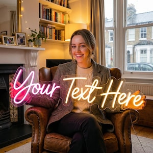 May include: A neon sign with the text "Your Text Here" in a flowing script. The sign has a pink and yellow glow and is held by a person. The sign is a decorative item.
