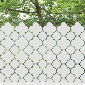 May include: A white frosted window film featuring a repeating quatrefoil pattern. The semi-opaque adhesive film covers the lower portion of a glass window pane, creating a decorative privacy screen with a scalloped top edge and clean lines.