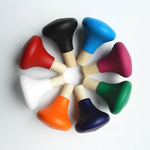 Op de afbeelding: Een verzameling van acht kleurrijke flessenstoppers, gerangschikt in een cirkel. Elke stopper heeft een houten basis en een geverfde bovenkant in verschillende kleuren: rood, wit, oranje, zwart, blauw, paars, groen en marineblauw. De stoppers zijn ontworpen voor wijnflessen.