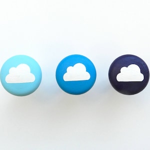 Può includere: Tre pomelli rotondi in legno con un design a nuvola bianca. I pomelli sono dipinti in tonalità di blu e viola.