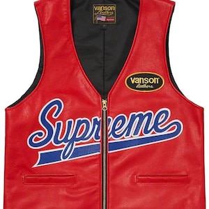 Puede incluir: Un chaleco de cuero rojo con interior negro y cremallera dorada. El chaleco presenta la palabra "Supreme" en escritura blanca con una línea azul. Tiene dos pequeños bolsillos y un parche de "Vanson Leathers".