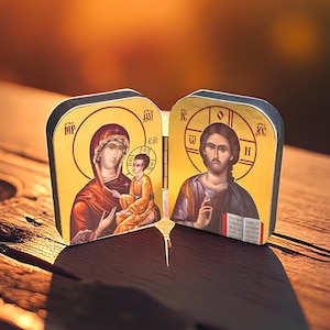 May include: Two wooden religious icons depicting religious figures. The icons feature gold backgrounds with images of the Virgin Mary and Jesus Christ. The icons are set on a wooden surface with a blurred background.