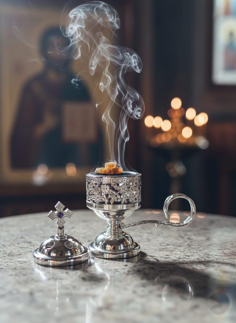 May include: A silver censer with detailed floral patterns, releasing plumes of smoke. The censer is placed on a marble surface, beside a silver lid with a cross. The background shows a blurred religious painting and candles.
