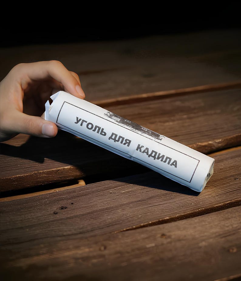 May include: A white paper-wrapped product with black text in Russian, held by a hand. The product is cylindrical and rests on a dark wooden surface. The text on the paper is partially visible.