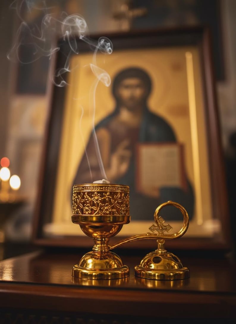 May include: A gold-coloured censer with floral detailing, emitting wisps of smoke. The censer is set against a backdrop of a religious icon, creating a serene and spiritual ambiance. The censer is a traditional item used in religious ceremonies.