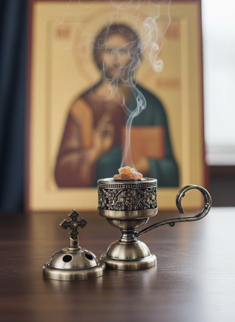 May include: An antique brass incense burner with a floral design, open, with a small cross-shaped lid next to it. Incense is burning, with smoke rising. A religious icon is in the background.