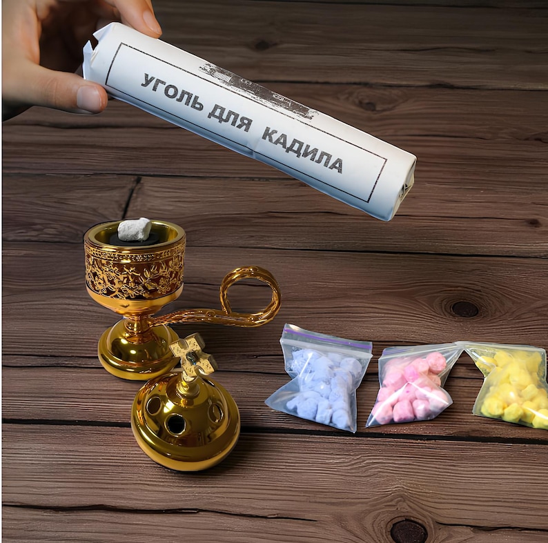 May include: A gold incense burner with decorative floral patterns, a cross-shaped base, and a handle. The image also shows a roll of paper with Cyrillic text, and small bags of blue, pink, and yellow incense.