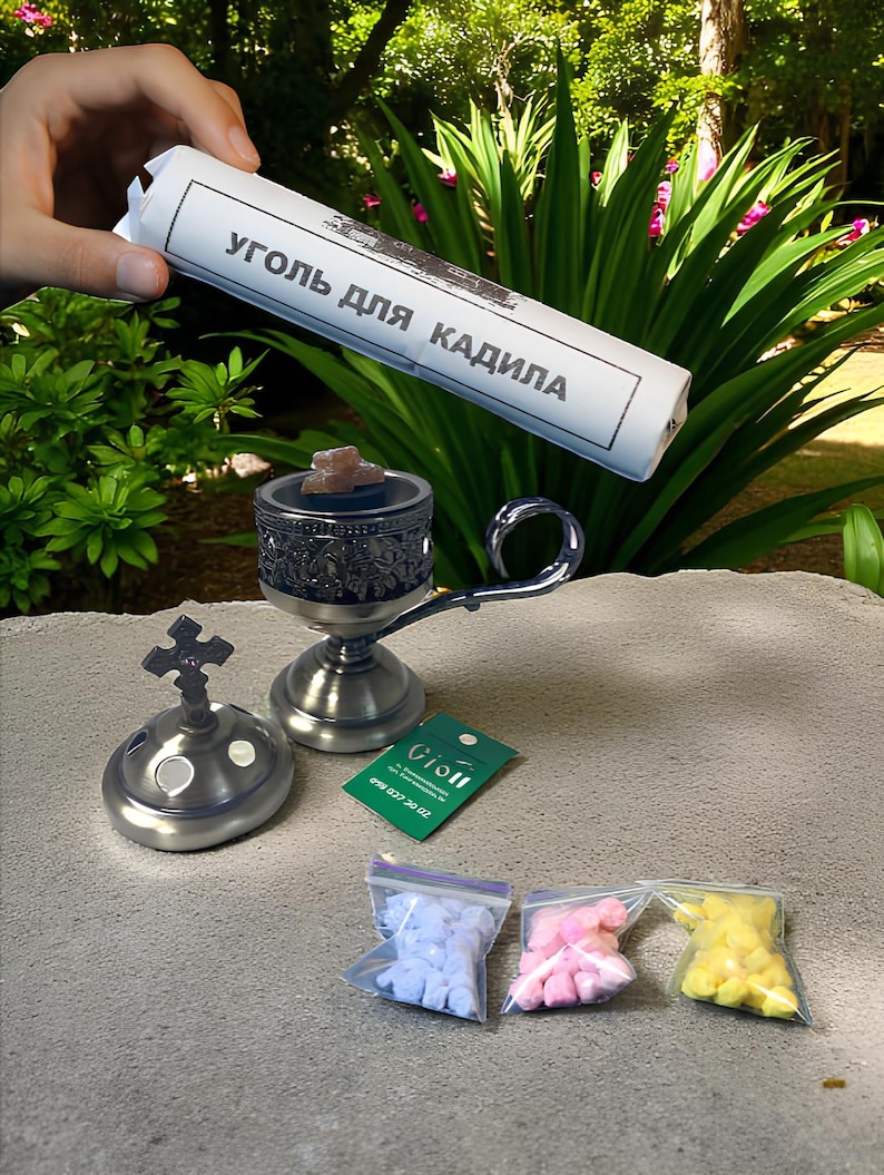 May include: A collection of religious items, including a silver incense burner with a cross-shaped top, a small censer, and three small bags of colourful incense. A roll of paper with Cyrillic text is held above the items.